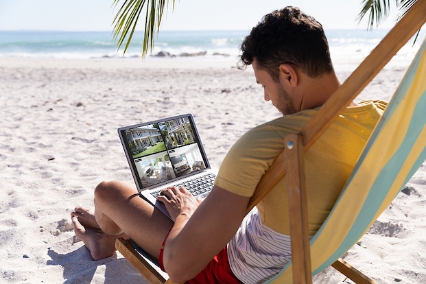 Man sitting on beach watching four security camera views on his laptop.